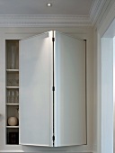 Glasses in fitted cupboard with modern folding door in traditional room with stucco ceiling