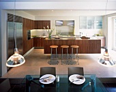 Open-plan kitchen with island and bar stools behind dining area