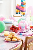 Fairy cakes, fresh strawberries and a birthday cake for children on a table with party decorations