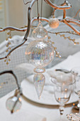Glass Christmas tree decorations hanging on twigs on set dining table