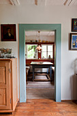 Doorway with wooden frame painted pale blue and view into rustic dining room beyond