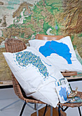 Kissen mit Landkartenmotiv auf Stühlen vor grosser Landkarte
