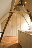 Schlichtes Dachzimmer mit Einbauschrank aus weiss lackiertem Holz an Giebelwand