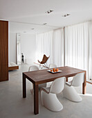 Minimalistisches Esszimmer mit Holztisch, weißen Stühlen und durchgehenden Vorhängen