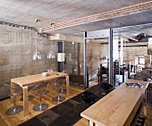 Holztische mit Designer-Stühlen in einer Küche mit Beton- und Glaswänden