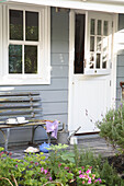 Bench and garden plants in front of blue-grey wooden house