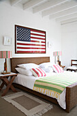 Schlafzimmer mit Rattanbett, gestreifter Bettwäsche und amerikanischer Flagge als Wanddekor