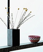 Shelf with twigs in concrete vase next to bowl with fish motif