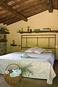 Schlafzimmer mit sichtbaren Deckenbalken, Metallbett und gemusterter Bettwäsche