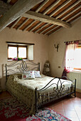 Metal bed with ornaments in rustic bedroom with beamed ceiling