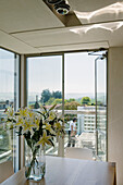 Vase with lilies on a table in a modern dining room with panoramic windows