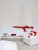 Bright red accessories and model sailing boat on wall combined with white covered chair and beanbag