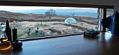 View of barren coastal landscape with sculptures and dome-shaped greenhouse through horizontal kitchen window