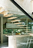 Offene Holztreppe mit gläserner Wange und Stahlträger vor Betonküche in zeitgenössischem Solarhaus