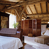 Rustic bedroom in the attic with wooden beams and louvre screen