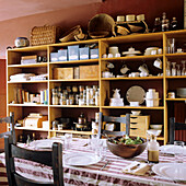 Set dining table in front of open wooden shelving wall with crockery and storage jars