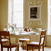 Set dining table with wooden chairs in front of window and ornate mirror