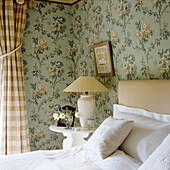 Bedroom with floral wallpaper and chequered curtains, side table with decoration