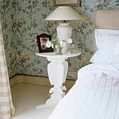 Bedside table with flowers and framed photo, floral wallpaper in the background