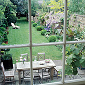 Blick auf Terrasse mit Tisch und Stühlen und gepflegten Garten mit Liegestuhl