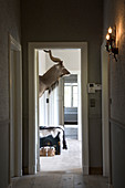 Stimmungsvolle Wandbeleuchtung im Flur und Blick durch offene Tür auf Tiertrophäe an Wand