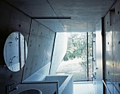 A bathroom with concrete walls, a round mirror and a glass partition wall
