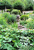 Stone pillar surrounded by a variety of green and flowering plants in the garden