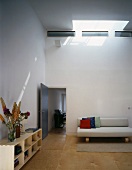 Purist living space with open-fronted sideboard and light sofa beneath skylight