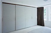 Fitted cupboards with white, sliding doors in designer bedroom