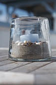 Light blue candle on bed of sand and shells in transparent candle lantern