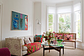 Bright living room with floral sofa, bouquet of flowers, cushions and blanket with floral pattern