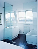 Glass partition in front of washstand and bathtub in white, modern bathroom