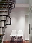 Retro chairs with white, plastic shell seats against wall in modern stairwell