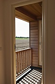 Modern wooden house with small balcony - sunlight falling through balustrade and view of farmland