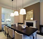 Modern dining area with pendant lamps in front of traditional fireplace beneath gilt-framed mirror