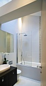 View through open door of bathtub with shower head behind glass partition in modern bathroom