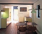 Open-plan, pastel yellow fitted kitchen with light dining furniture and industrial-style wall lamp