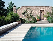 Pool with wooden decking sheltered by brick wall with creepers and doorway with wooden door
