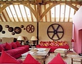 Converted barn with pink sofas and antique table against half-height partition with old cogwheels
