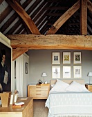 Modern bedroom with light wooden furniture beneath old, heavy roof timbers