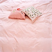 Zwei Zierkissen auf rosa Bettwäsche