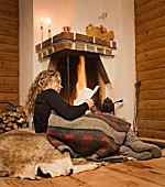 Woman lying in front of fire on fur reading book