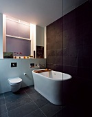 Free-standing bathtub on grey tiled floor in front of dark grey wall