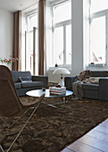 Fifties-style grey upholstered sofa set and coffee table on brown rug in traditional setting