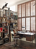 Vintage style desk below window with closed shutters next to shelves with collectors' items