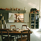 Wooden table and rustic shelves with crockery in country house kitchen