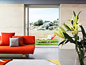 Floor-to-ceiling open sliding doors between wall segments and an orange designer sofa