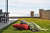 Ein rotes Kissen und ein Hut auf einer Rasenfläche mit Blick aufs Meer