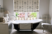 Free-standing, vintage bathtub in front of window with blind in modern setting