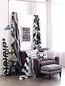 Black and white patterned lengths of fabric next to upholstered armchair with scatter cushions and footstool